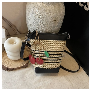 Detail of raffia woven bucket bag with black leather trim and cherry charm accessory