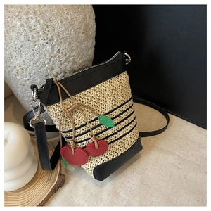 Detail of woven straw shoulder bag with black stripes and decorative red cherry charm