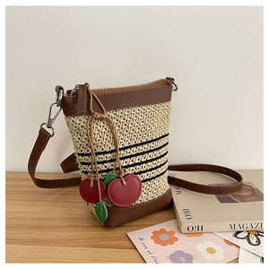 Detail of raffia woven crossbody bag featuring red cherry charms and brown leather trim