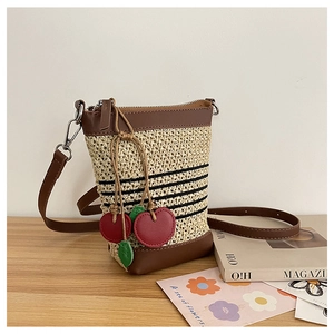 Detail of straw woven crossbody bucket bag with red cherry charms on wooden table