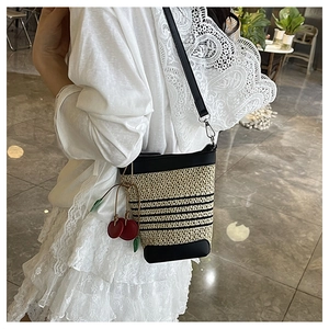 Detail of raffia woven bucket bag with black leather trim and cherry charm decoration