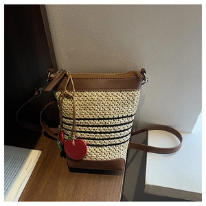 Detail of beige raffia bucket bag with brown leather trim and red cherry charm