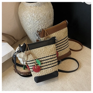 Detail of woven straw crossbody bag with striped pattern and cherry pendant charm
