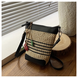 Detail of raffia woven crossbody bag with black leather trim and cherry charm on wood