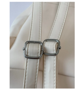 Close-up of adjustable straps and silver metal buckles on a cream leather backpack