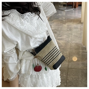 Detailed straw woven crossbody bag with black stripes and a red cherry charm decoration