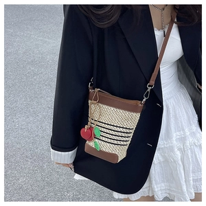 Detail of woven raffia crossbody bag with cherry charm and brown leather trim accents