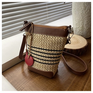 Detail of raffia woven crossbody bag with leather trim and red cherry charm