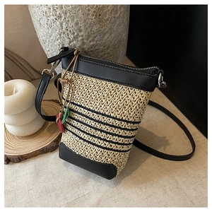 Detailed texture of woven raffia crossbody bag with black leather trim and leaf charm