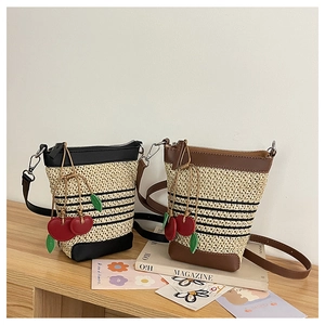 Detail of straw bucket bags with leather trim and cherry charm on a wooden surface