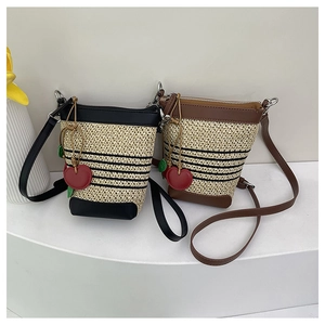 Detail of woven straw bucket bags with leather trim and cherry charms on a white stand
