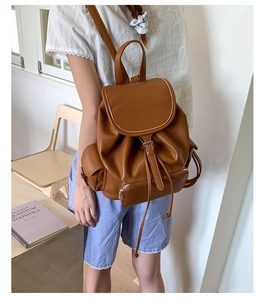 Brown leather backpack on a student desk showing vintage buckle and front zipper pocket