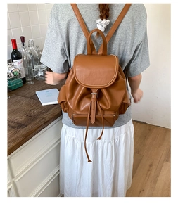 Rear view of a vintage brown leather backpack worn by a model in a kitchen setting