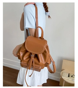 Detail of brown leather backpack featuring a vintage metal buckle and drawstring closure