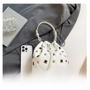Detailed top view of white studded bucket bag with silver chain on grey fabric