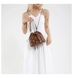 Close-up of brown leather bucket bag with silver studs and chain strap on a model