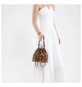 Detail view of brown leather bucket bag with silver metal eyelets and rivets decoration