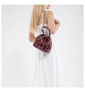 Detail of burgundy drawstring bucket bag with silver studs worn by a model in a white dress