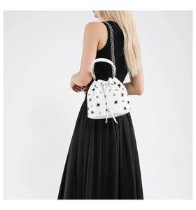 White leather bucket bag with silver studs on model wearing black dress