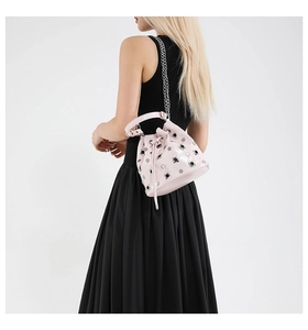 Detail view of light pink bucket bag with silver studs and chain strap on a model