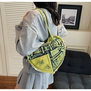 Detail of heart-shaped denim shoulder bag with frayed edges and metal buckle in yellow-green