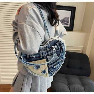 Detail of heart-shaped denim shoulder bag featuring distressed edges and pocket elements