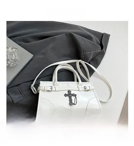 Detailed macro view of white patent leather bag with vintage metal cross and chain ornament