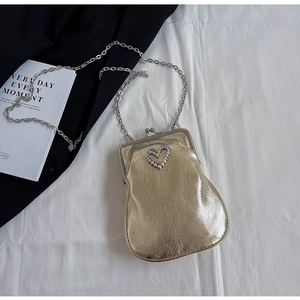 Detail view of golden crossbody bag featuring a pearl-inlaid hollow heart on metal texture