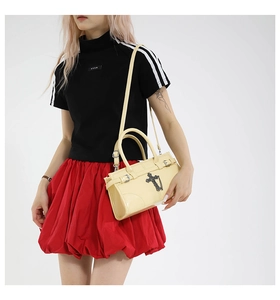 Detail of light yellow glossy handbag with metallic cross charm and chain strap