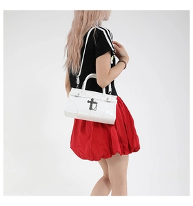 Detail of white glossy leather handbag with vintage metal cross and chain accessory