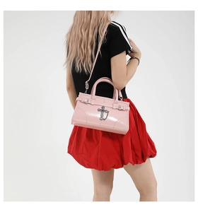Pink patent leather handbag with silver cross charm and buckle straps shown on a model