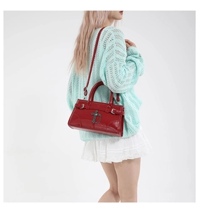 Close-up of a red patent leather crossbody bag featuring Gothic cross charms and chain