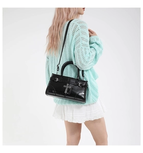 Side view of black gothic handbag with silver cross and chain on mint green sweater