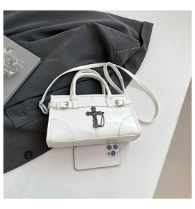 Close-up of white leather Boston bag featuring vintage cross metal decor and chain charms