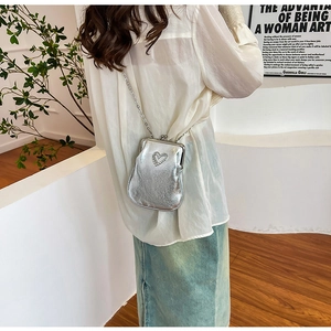Detail of silver chain strap on mini crossbody bag featuring a heart pattern finish