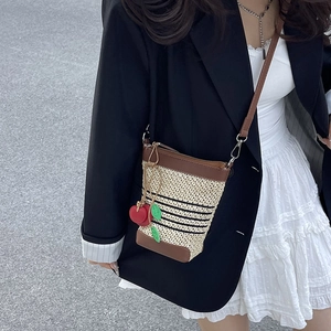 Straw bucket crossbody bag with cherry charm and brown leather trim on model