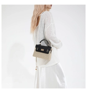 Détail d'un sac bandoulière en paille avec rabat en cuir noir et fermoir doré porté par mannequin