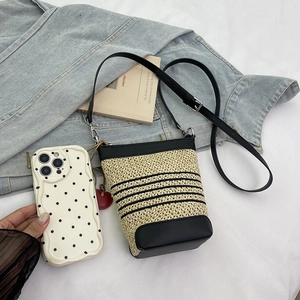 Raffia bucket bag with black stripes and leather strap shown on casual denim background