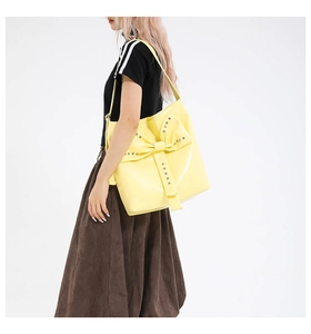 Detail view of bright yellow patent leather tote with oversized bow and silver metal rivets
