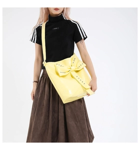 Detail of yellow patent leather shoulder bag featuring large bow and metal rivets