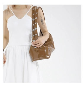Detail of a brown glossy hobo bag featuring wide shoulder straps and silver metal studs