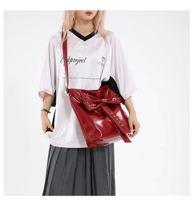 Detail of red patent leather tote bag with a large bow and silver metal rivets decoration