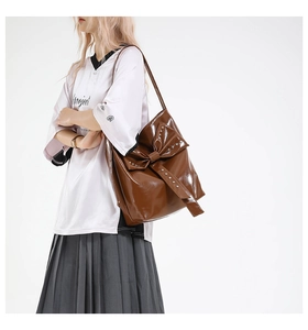 Close-up of caramel patent leather tote bag with rivet bow detail on a model