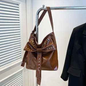 Detailed view of brown tote bag featuring a large crystal-embellished bow on glossy leather