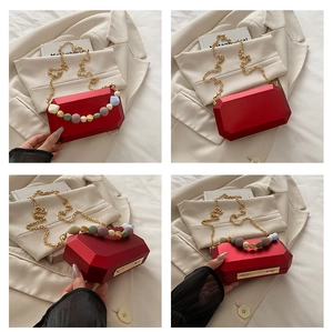 Λεπτομέρεια κόκκινης γεωμετρικής τσάντας clutch με χρυσή αλυσίδα και πολύχρωμες χάντρες