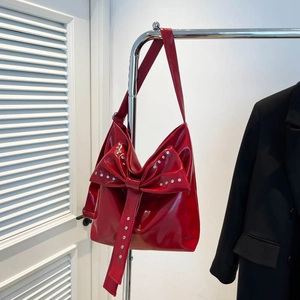 Detailed view of the large red bow and silver rivets on the glossy patent leather tote