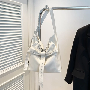 Detail of white tote bag featuring large bow and silver studs on glossy faux leather