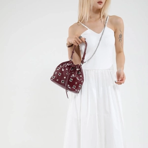 Dark red bucket bag with silver studs and chain strap shown on model over white background