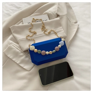 Detail of royal blue acrylic box bag with colorful beads and gold chain on beige background
