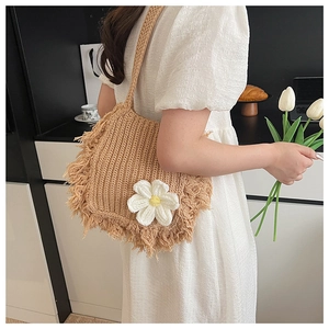 Close-up of khaki woven shoulder bag featuring white crochet flower and tassel details